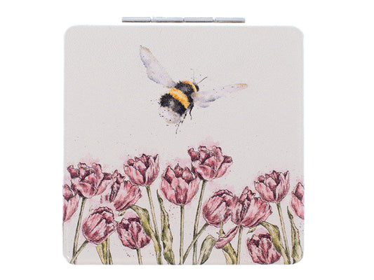 a light pink pocket mirror with pink flowers around the base and a bee flying above them